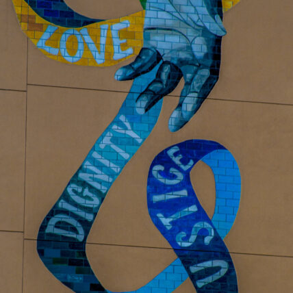 mural of hand and text of justice, dignity, love on blue ribbon