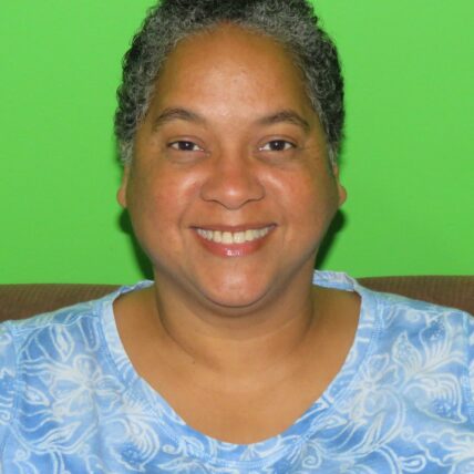 Headshot of Deborah Berry, a Black person wearing blue shirt against a green background. Her hair is short and curly, she smiles at the camera.